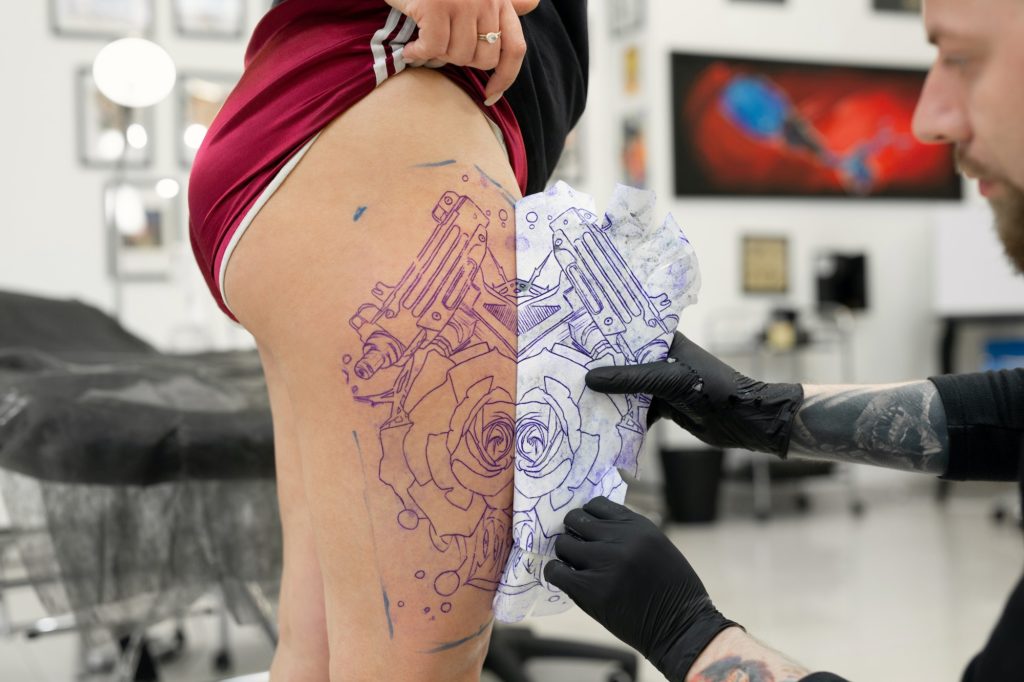 Tattoo artist transferring a tattoo sketch to a woman leg in a tattoo parlor